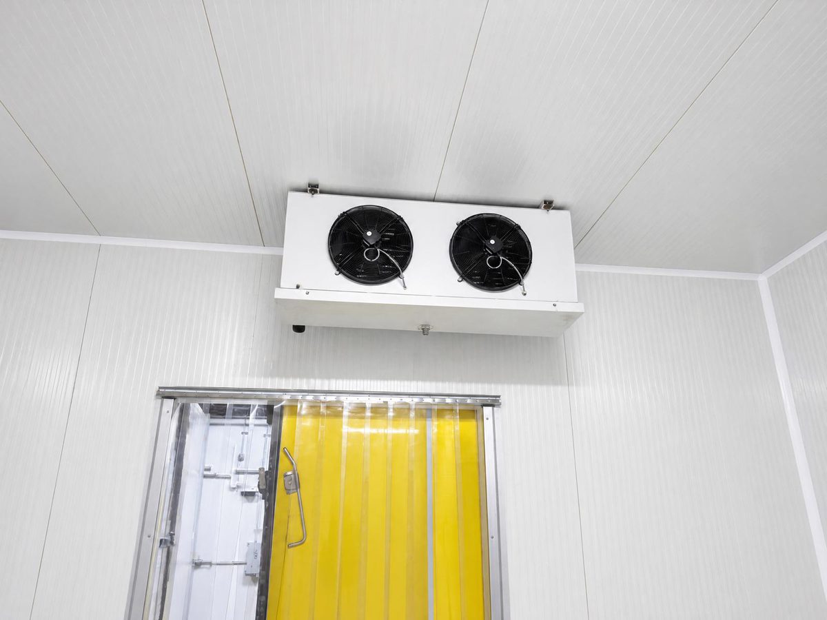 Ceiling-mounted evaporator unit above a cold room doorway with a strip curtain