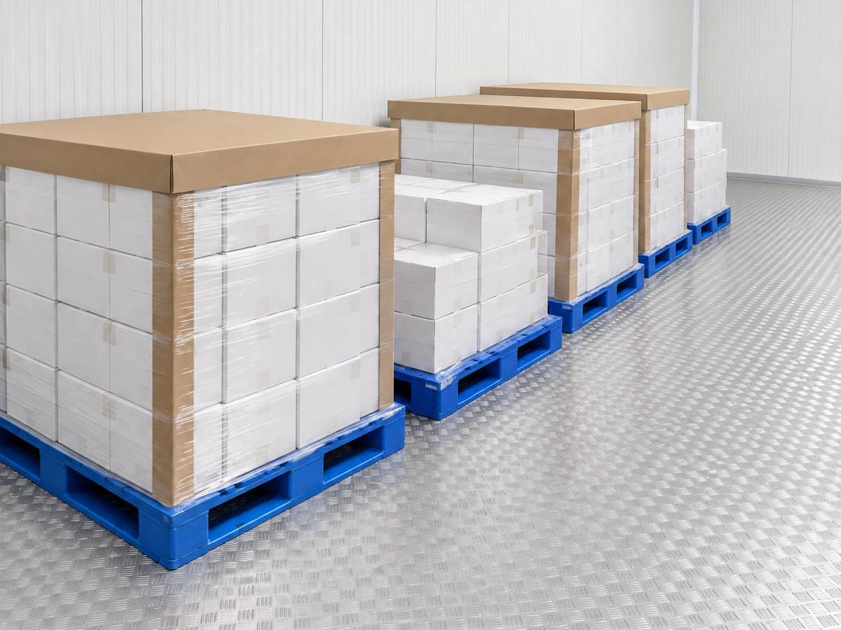Inside a cold room: shrink-wrapped boxed goods stacked on blue plastic pallets